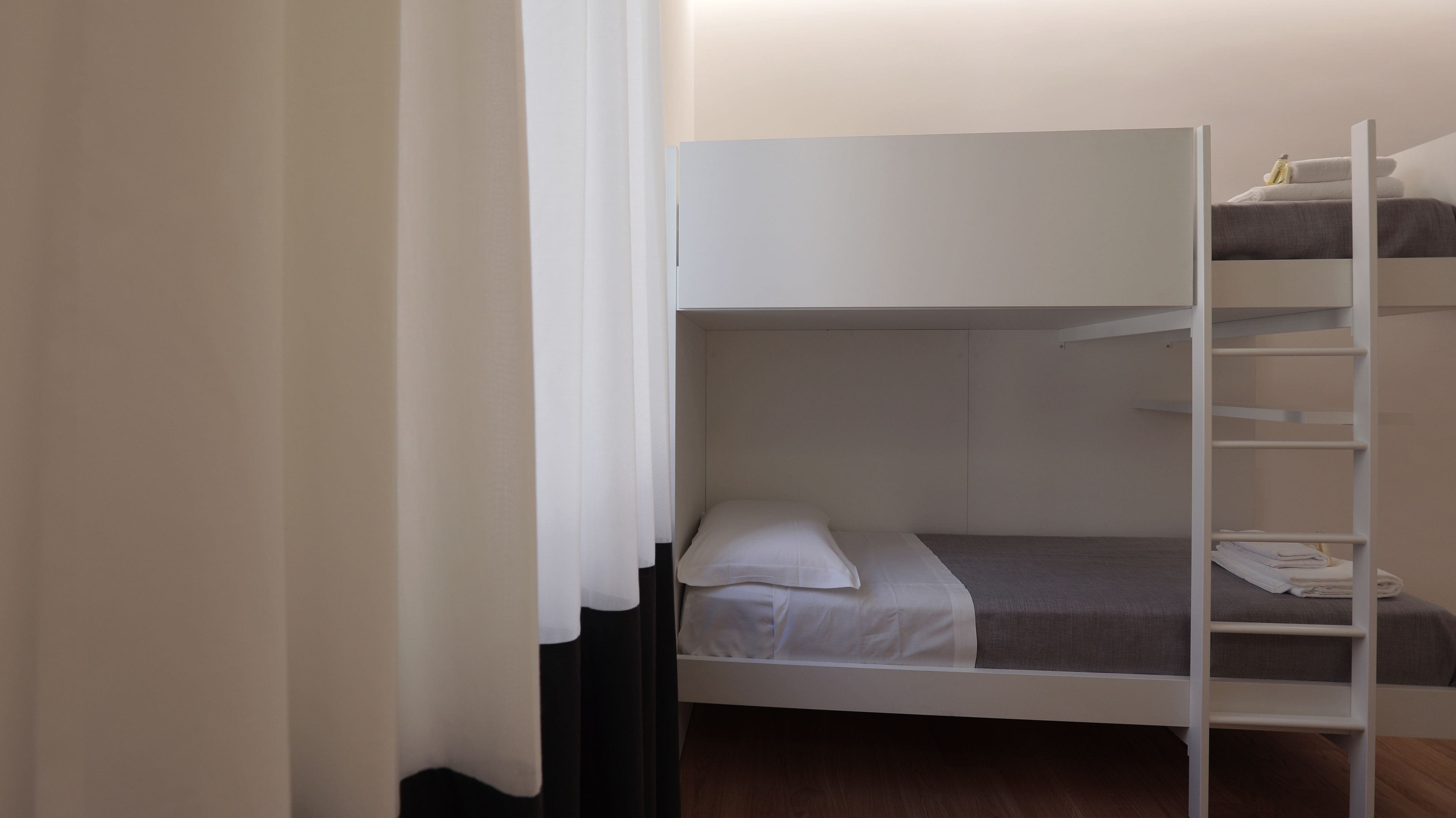 A bunk bed with a ladder, a white curtain, and a small shelf with towels.