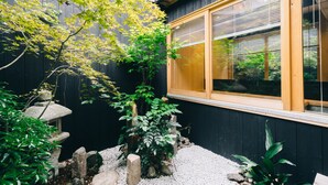 Un jardin japonais traditionnel agrémenté d’une lanterne en pierre, d’un bonsaï et d’une fenêtre en bois dotée de panneaux coulissants de type shoji.