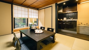 Une pièce de style japonais traditionnel, avec un sol recouvert de tatamis, une table basse avec des coussins, une porte coulissante et une vue sur un jardin.