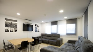 A modern living room with a sofa, a dining table, and chairs. There are pictures on the wall and a flat-screen TV mounted above the sofa. - Residencia Universitaria Alboran (Málaga)