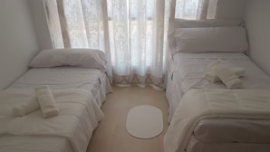 A room with two beds, each with white bedding and pillows, a small round rug on the floor, and sheer curtains with a floral pattern. - Residencia Universitaria Alboran (Málaga)