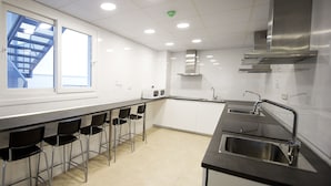 A modern kitchen with a bar area, stainless steel appliances, and a view of a building outside. - Residencia Universitaria Alboran (Málaga)