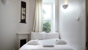 Hotellihuone, jossa on sänky, takka, ikkuna verhoilla ja seinälle ripustettu taideteos.
