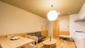 A compact living space with a wooden dining table, sofa, and bench. A small round table with a vase of flowers is in the center. - Miro Sanjo Saiin Tei (Kyoto)