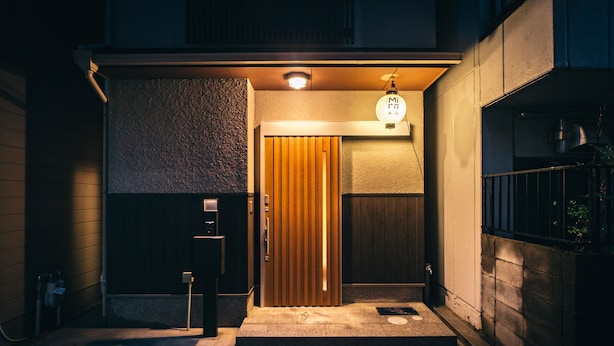 A well-lit entrance with a wooden door, a small step leading up to the door, and a light fixture above. - Miro Sanjo Saiin Tei (Kyoto)