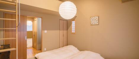 Un dormitorio con cama, una escalera, una lámpara colgante y un ventanal pequeño.
