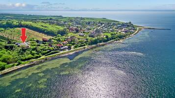 Une vue aérienne d’une ville côtière, avec une vue dégagée sur la mer, des collines verdoyantes et une flèche rouge indiquant un endroit précis.