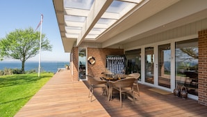 A deck with a table and chairs, overlooking a body of water, with a flagpole and a view of the sea.