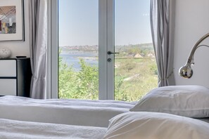 A bedroom with a large window, a bed, a bedside table, and a lamp. - Fjordhuset (Broager)