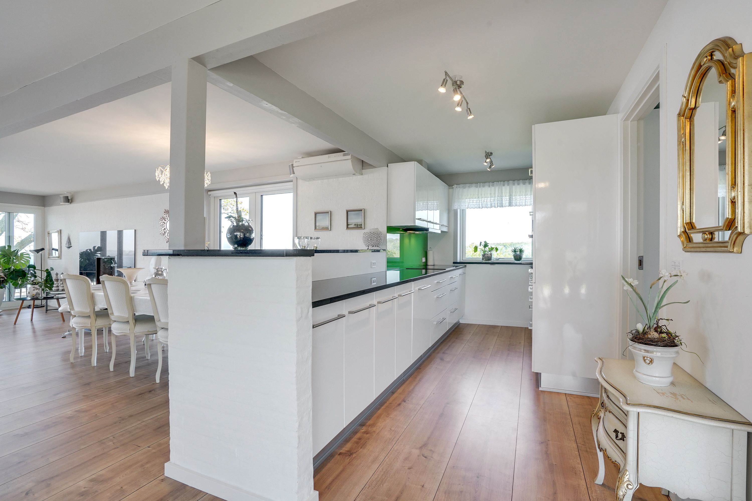 Une cuisine spacieuse avec des meubles blancs, un îlot central et un coin repas doté de chaises blanches.