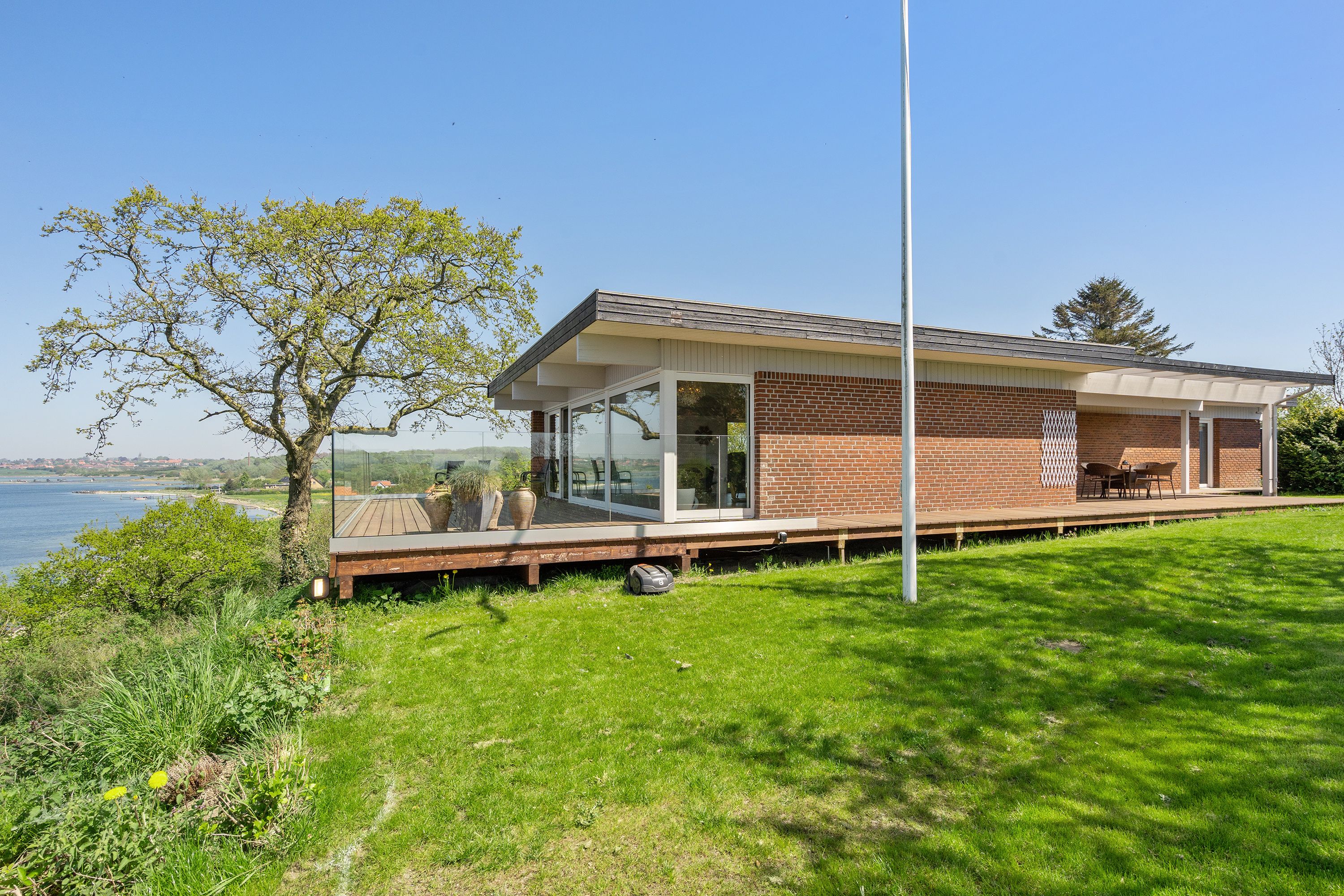 A modern house with a glass extension, a deck, and a view of the water.