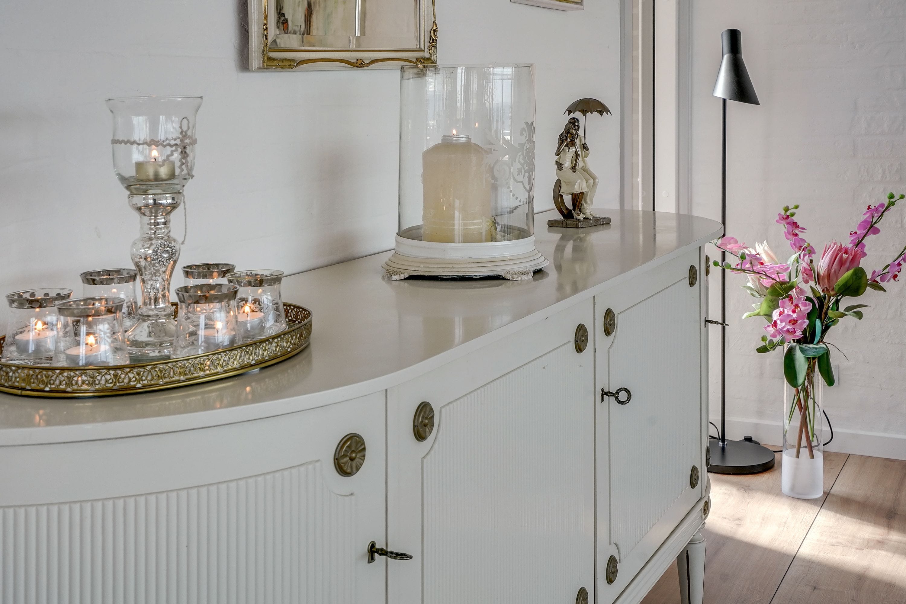 A white cabinet with glass candle holders and a lit candle.