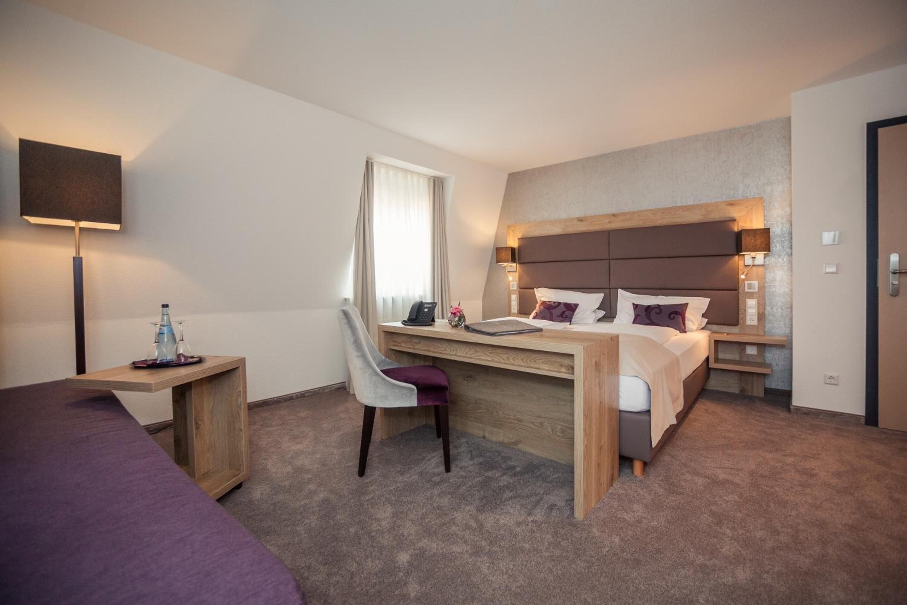 Una habitación de hotel con cama, escritorio, silla, lámpara y televisor.