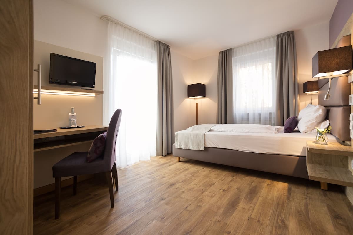 Une chambre d’hôtel moderne équipée d’un lit, d’un bureau, d’une chaise, d’une télévision et de lampes de chevet.