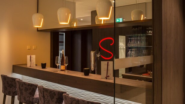 Eine moderne Bar mit Holztresen, Barhocker und hängenden Pendelleuchten.