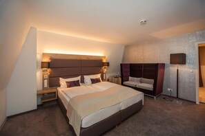 Una habitación de hotel moderna con una cama grande, mesitas de noche, un sofá y una lámpara.