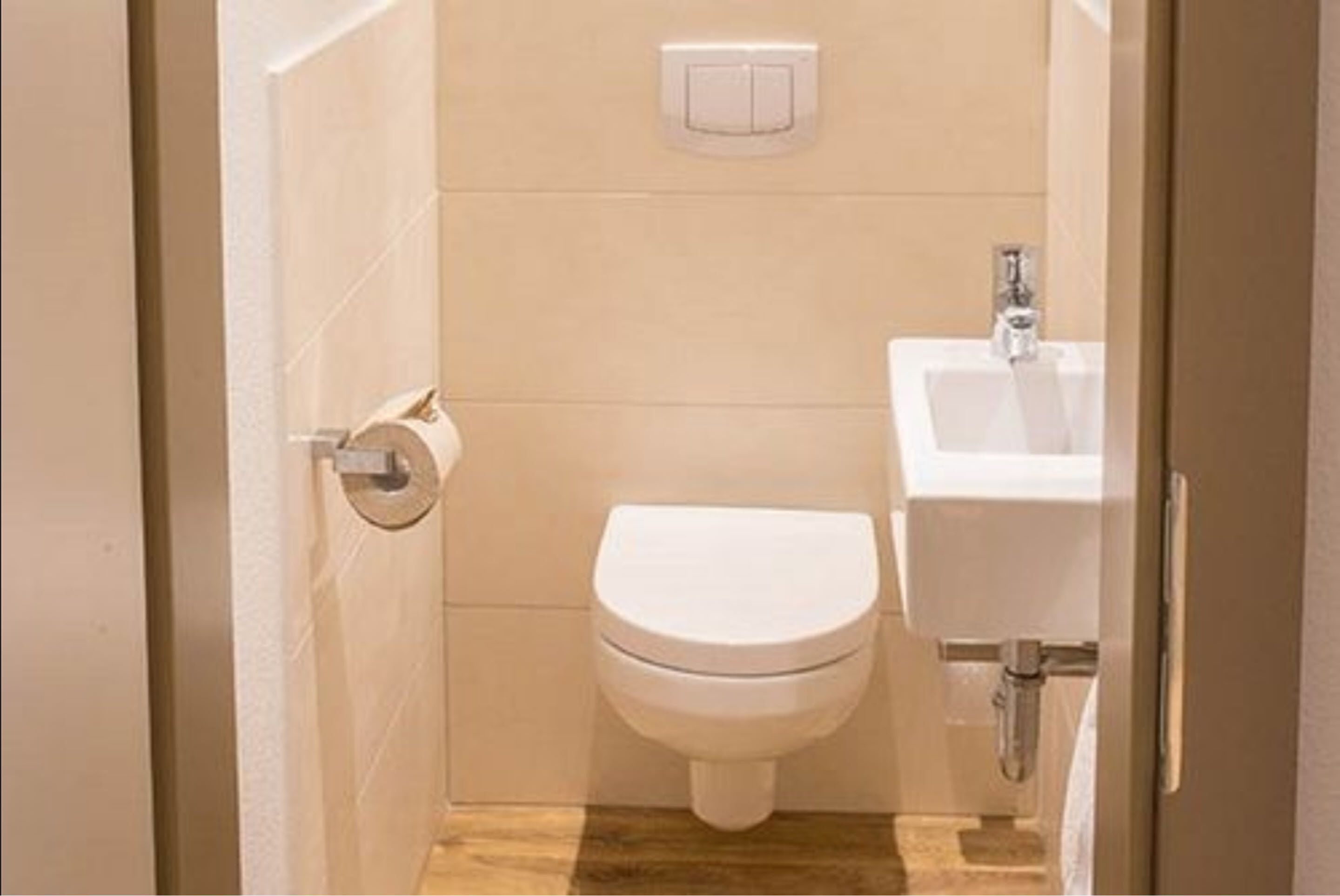 A small, compact bathroom with a toilet, a sink, and a toilet paper holder.