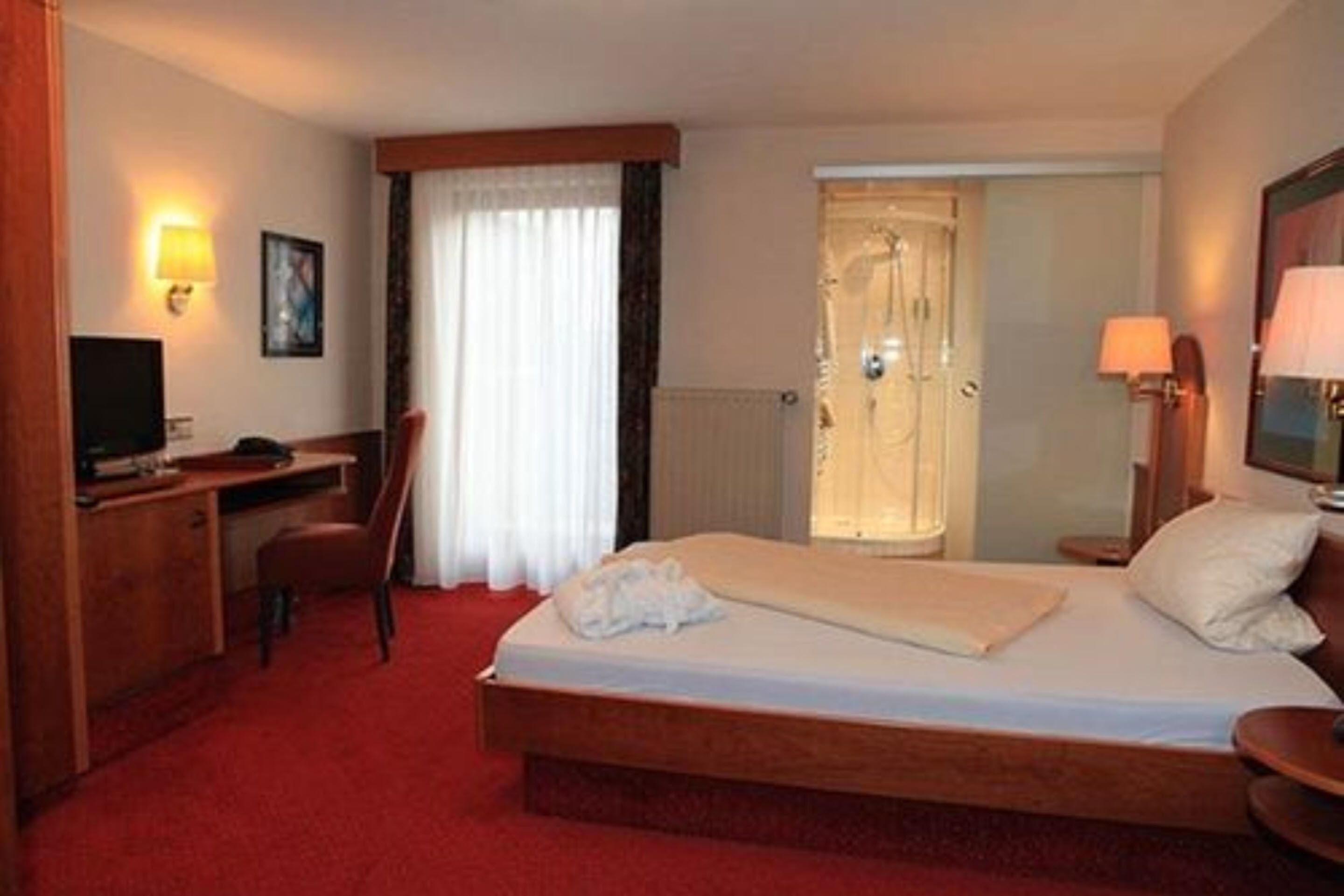 Ein Hotelzimmer mit Bett, Schreibtisch, Stuhl, Fernseher und einer Tür zu einem Badezimmer.