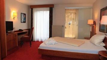 Ein Hotelzimmer mit Bett, Schreibtisch, Stuhl, Fernseher und einer Tür zu einem Badezimmer.