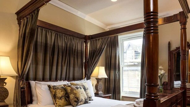 Ein Himmelbett mit Baldachin, Holzboden, Teppich und ein Fenster mit Vorhängen.