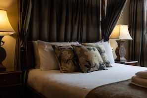 Una cama con dosel, almohadas estampadas con motivos florales, una mesita de noche con lámpara y un dosel superior.
