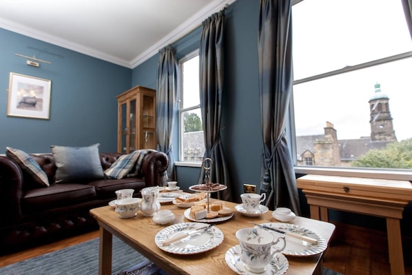 Una habitación con una mesa puesta para tomar el té, un sofá de cuero marrón y vistas a un paisaje urbano a través de una ventana.