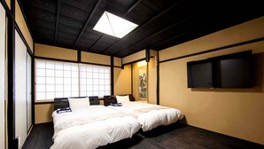 Een hotelkamer met twee bedden, een groot raam, een plafondlamp en een flatscreen televisie aan de muur.