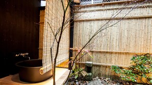 Een traditionele Japanse tuin met een stenen hottub, een bamboebeschutting en een kleine boom.