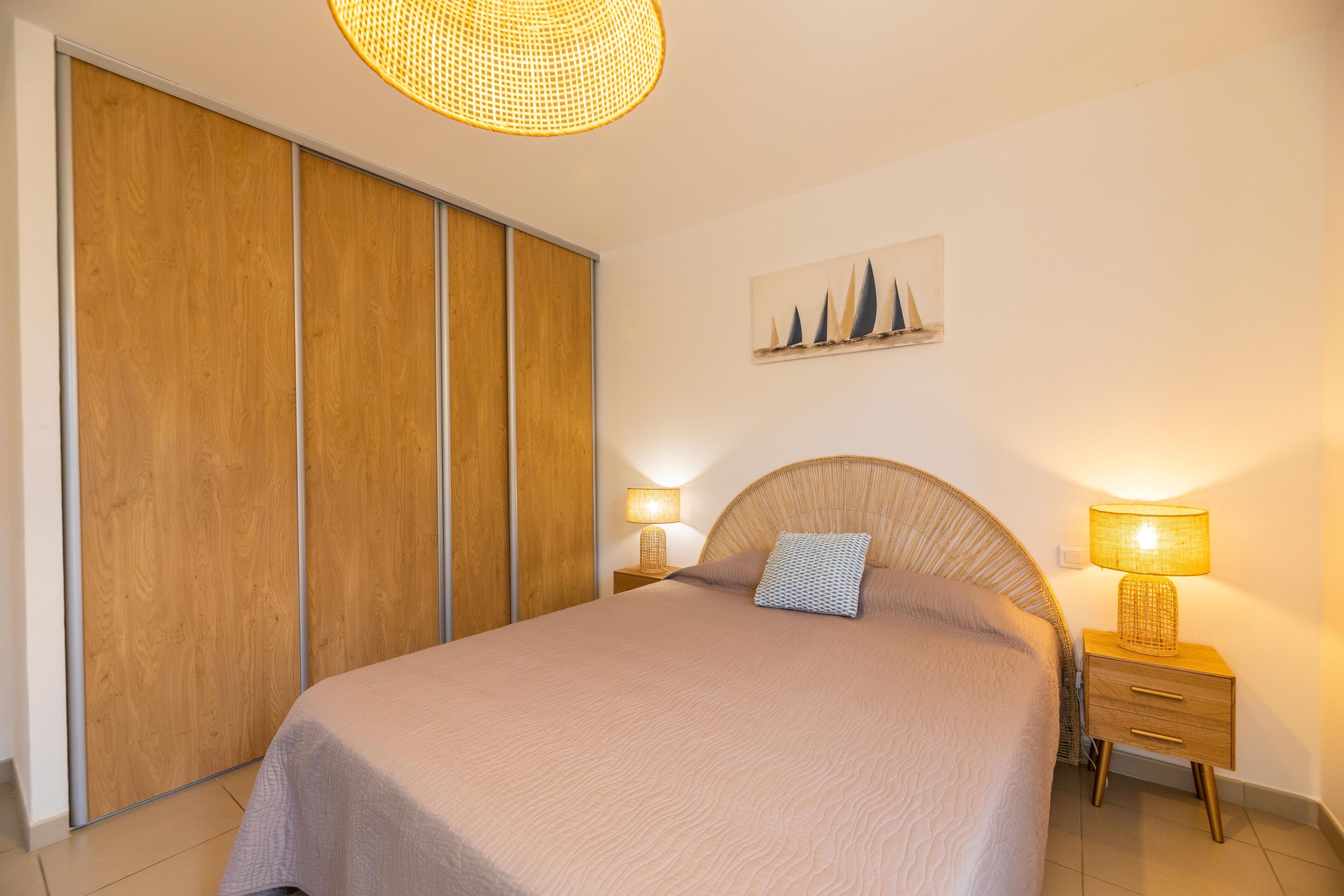 Ein Schlafzimmer mit Bett, Holzschrank, Nachttischlampen und einem an der Wand hängenden Kunstwerk.