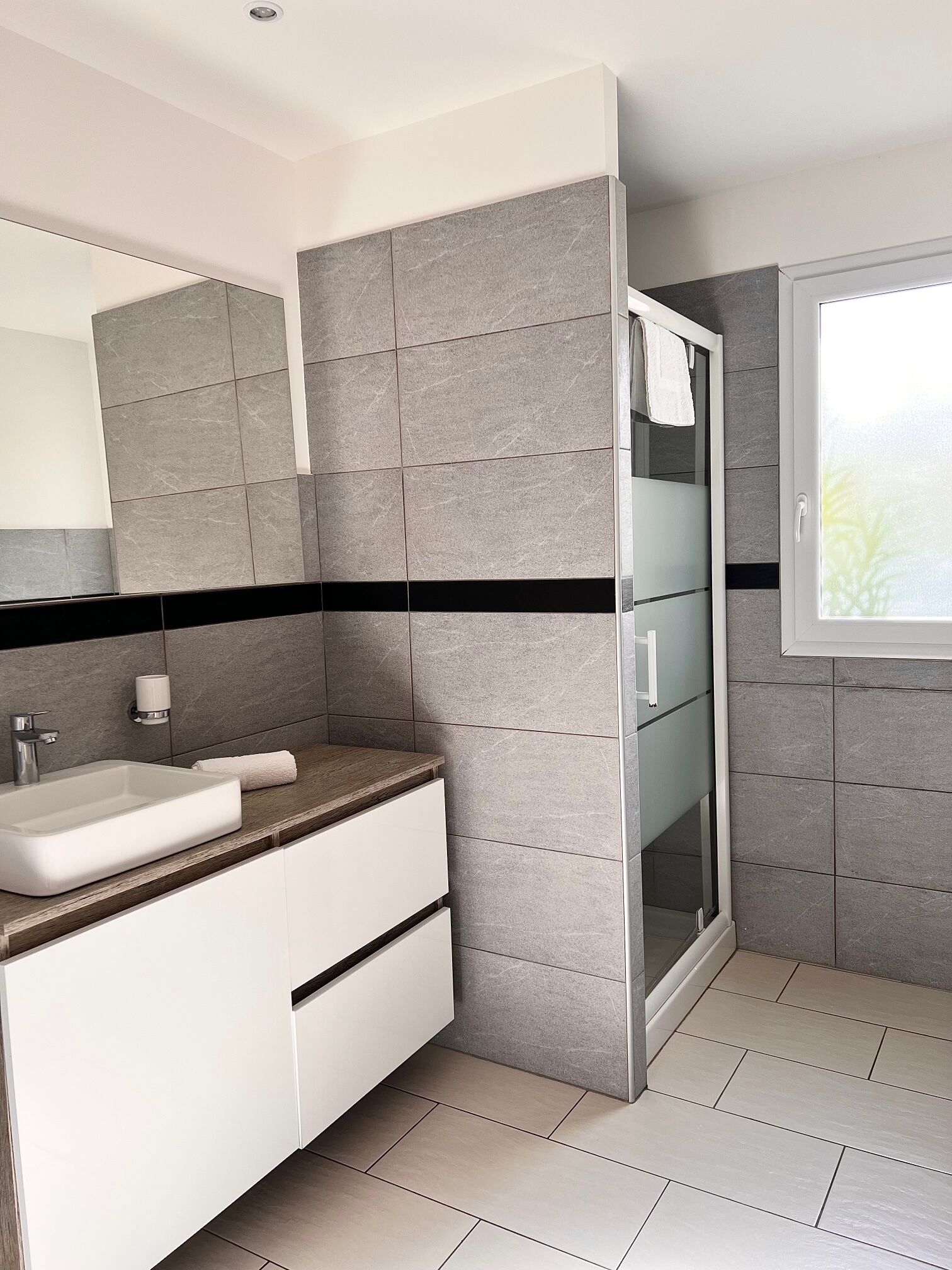 Une salle de bain moderne avec un lavabo rectangulaire, un miroir et une cabine de douche en verre.