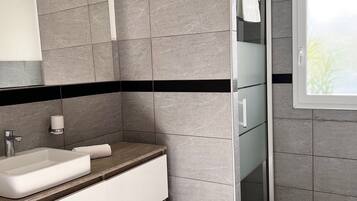 A modern bathroom with a rectangular sink, a mirror, and a glass shower enclosure.