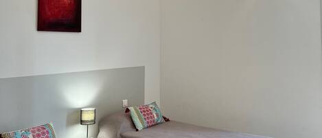A room with two beds, a nightstand, a lamp, a red abstract painting, and a ceiling light fixture.