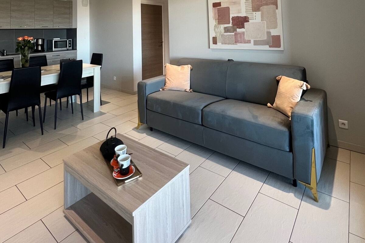 A modern living room with a grey sofa, a coffee table, and a dining area with chairs and a table.