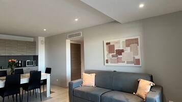 Uma sala de estar moderna com um sofá cinzento, uma mesa de centro e um espaço de jantar com cadeiras e uma mesa.