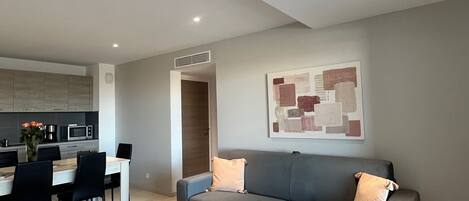 Un salon moderne avec un canapé gris, une table basse et un coin repas comprenant des chaises et une table.