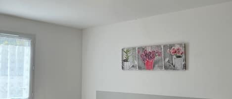 A bedroom with two beds, a ceiling light fixture, a window with curtains, and a wall-mounted artwork.