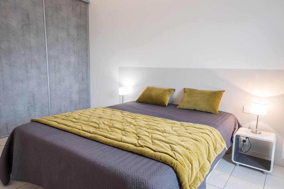 A modern bedroom with a large bed, two pillows, a bedside table with a lamp, and a wardrobe.