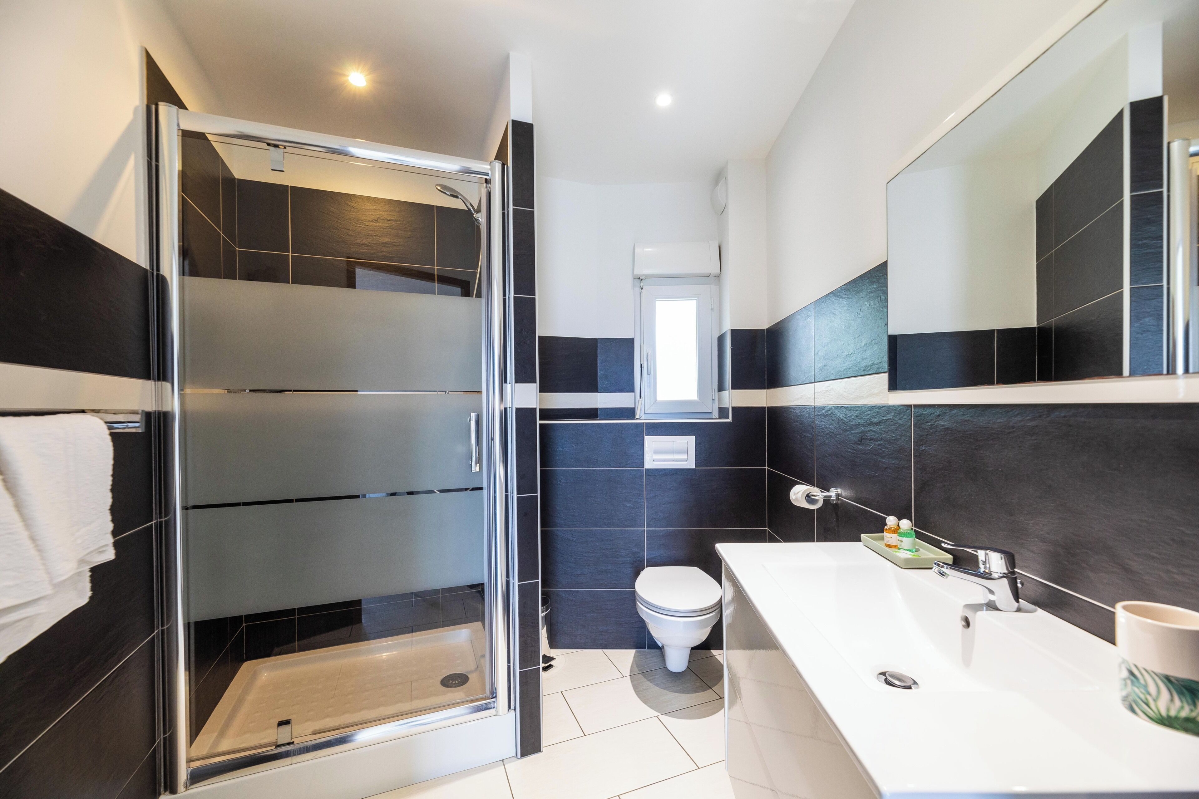 A modern bathroom with a glass shower enclosure, a white sink, and a large mirror.
