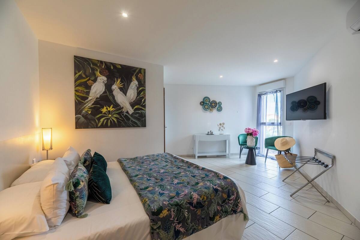 A bedroom with a bed, a painting of birds, a desk, and a chair.