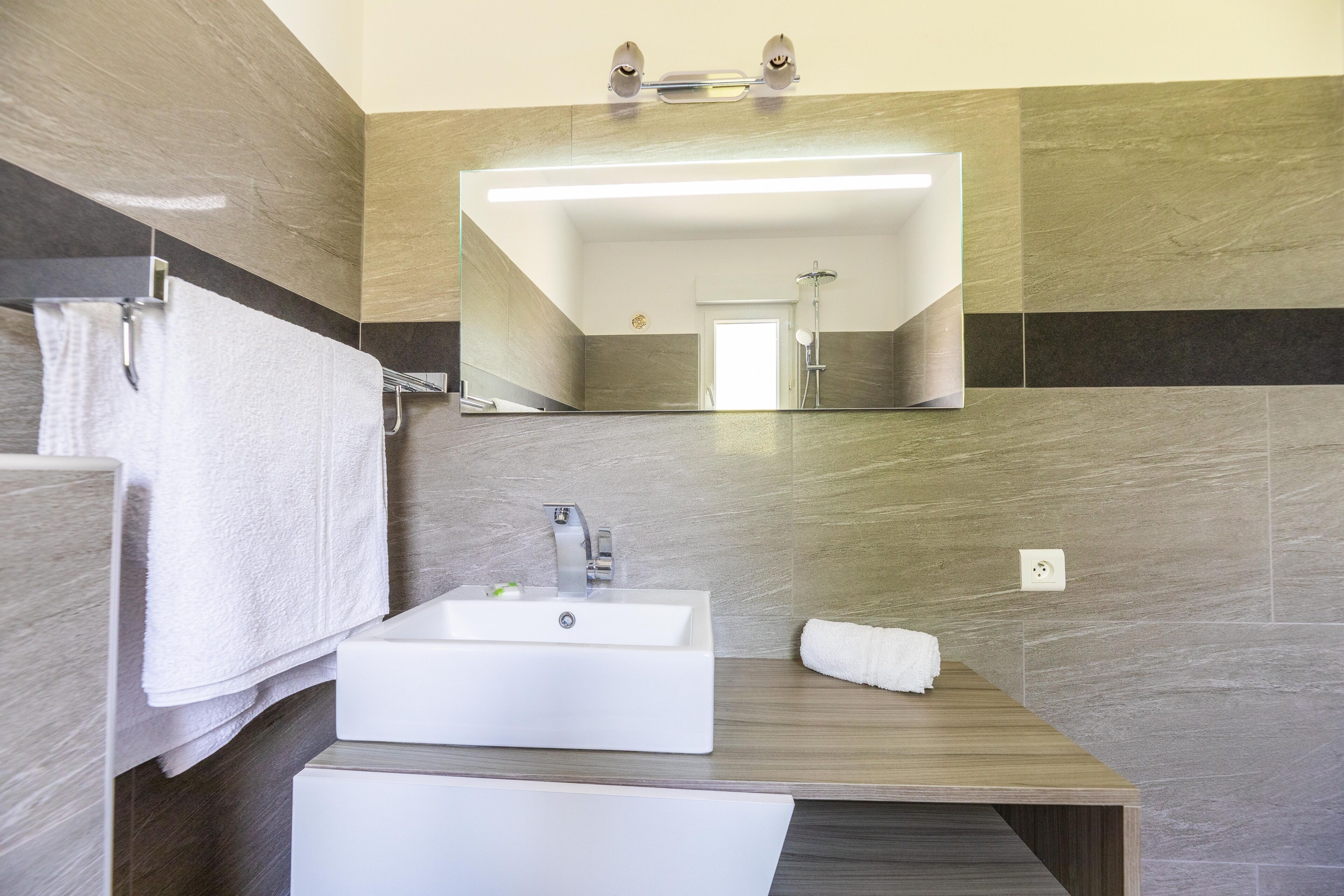 Uma casa de banho moderna com um espelho grande, uma pia e um chuveiro.