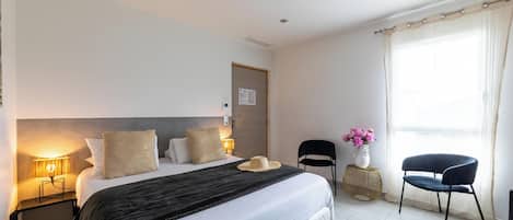 A hotel room with a large bed, bedside lamps, a chair, a small table with flowers, and a window with curtains.