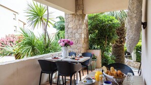 An outdoor dining area with stone walls, black chairs, a table with plates, a vase of flowers, and a view of greenery and buildings. - Les Alizés Résidence & Spa  (Monticello)