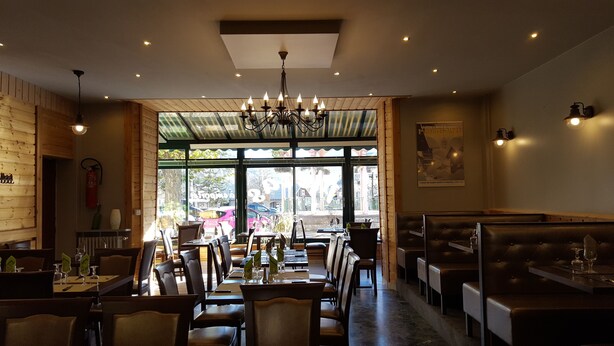 A restaurant with wooden walls, a chandelier, and large windows offering a view of the street. - Hôtel Restaurant Glaizette (L'Argentiere-la-Bessee)