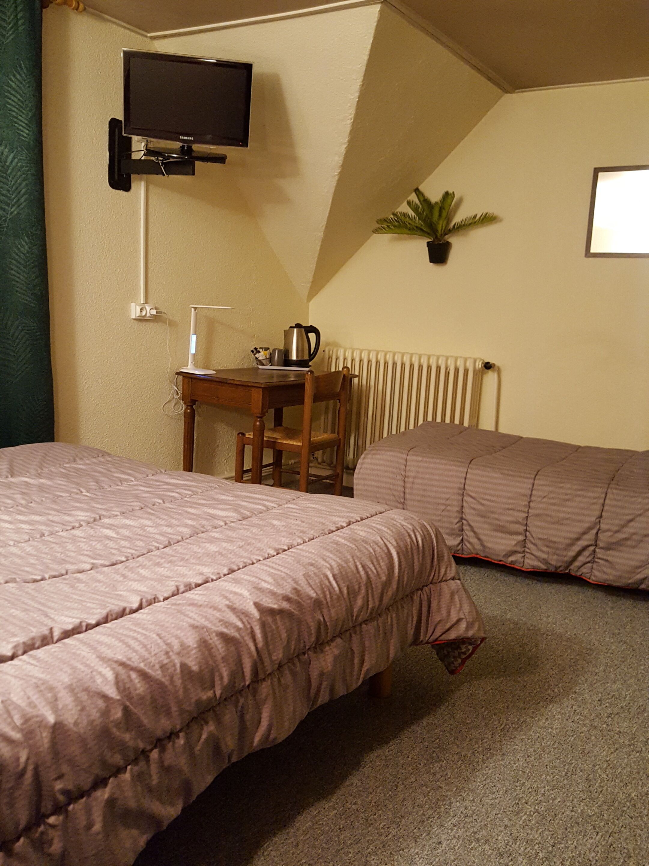 A hotel room with two beds, a desk with a lamp, a television, and a radiator.