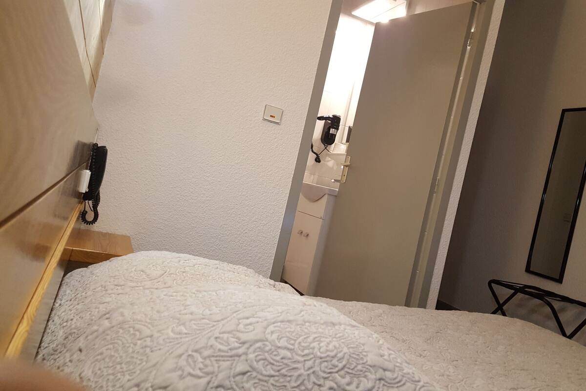 A hotel room with a bed, a bedside table, a mirror, and a door leading to a bathroom.