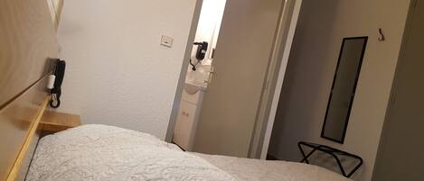 Una habitación de hotel con una cama, una mesita de noche, un espejo y una puerta que da a un baño.