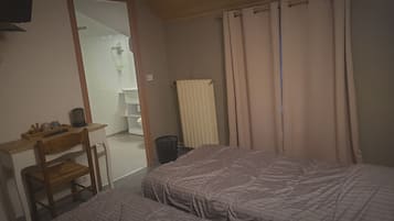 Un dormitorio con dos camas, un escritorio con silla, un radiador y un baño visible a través de una puerta abierta.
