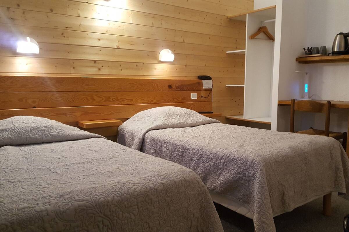 A room with two beds, wooden walls, a shelf with kitchen items, and a hanging rack.
