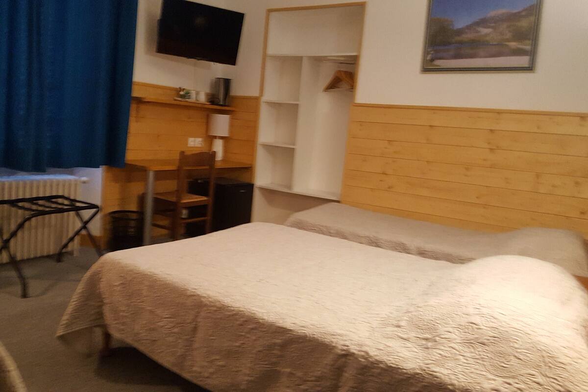 A room with two beds, a desk, a chair, a radiator, and a television mounted on the wall.