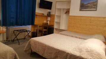 A room with two beds, a desk, a chair, a radiator, and a television mounted on the wall.